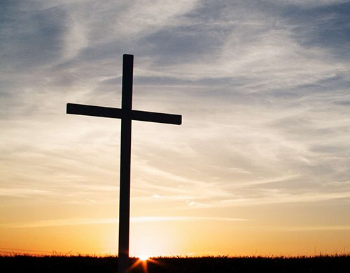 a christian cross symbol silhouette at sunset sunrise.